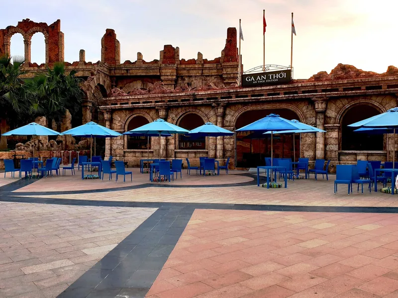 Blue umbrellas and tables sit before the weathered Roman-style ruins of An Thoi Station in Phu Quoc.