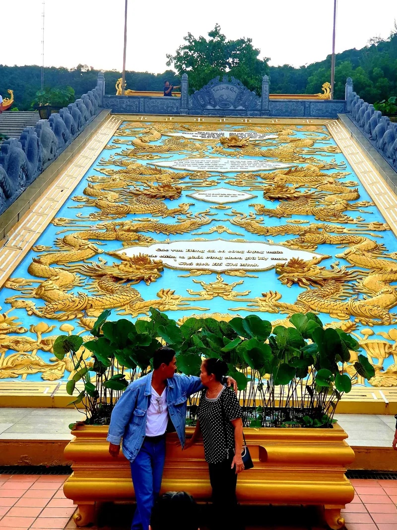 A couple poses before an elaborate gold dragon relief carving at Ho Quoc Pagoda in Phu Quoc.