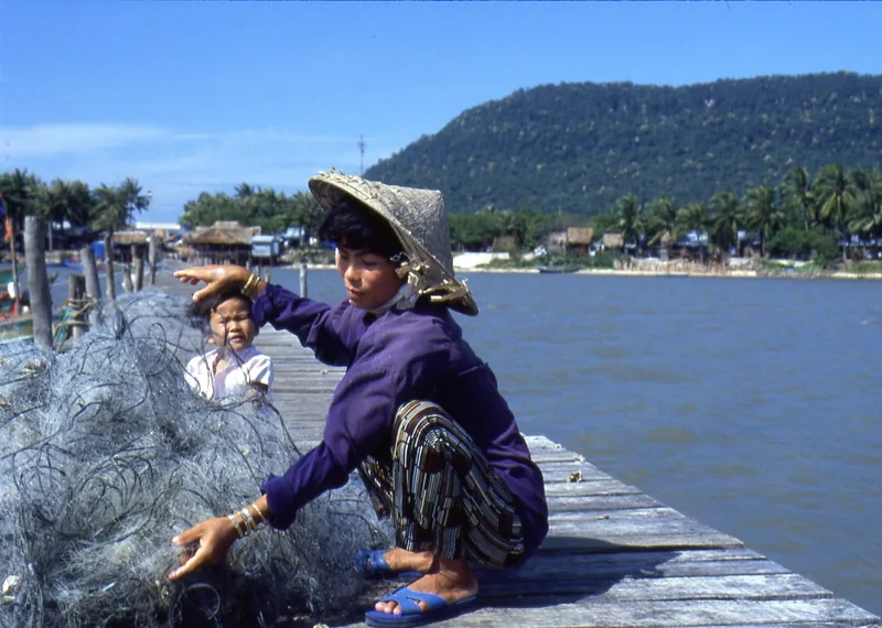 A fisherwoman in a conical hat mends nets on a wooden pier near a village in Phu Quoc.