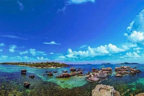 Rocky outcrops rise from turquoise waters off a green islet near Phu Quoc under a vivid blue sky.