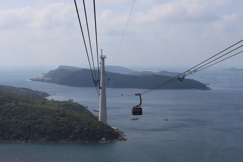 A cable car gondola glides over the sea toward Hon Thom island near Phu Quoc, with a tall tower pylon in the foreground.