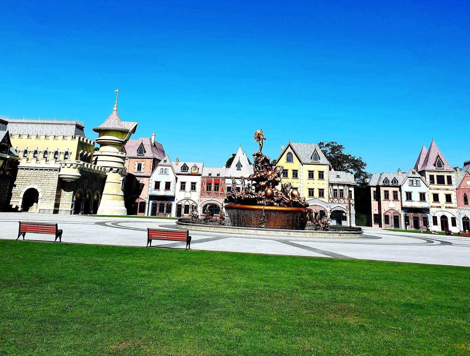 A European-style plaza with colorful gabled houses and a bronze fountain under a clear blue sky in Phu Quoc.
