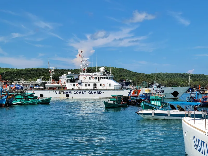 A Vietnam Coast Guard patrol vessel is docked among fishing boats in a harbor near Phu Quoc under a blue sky.