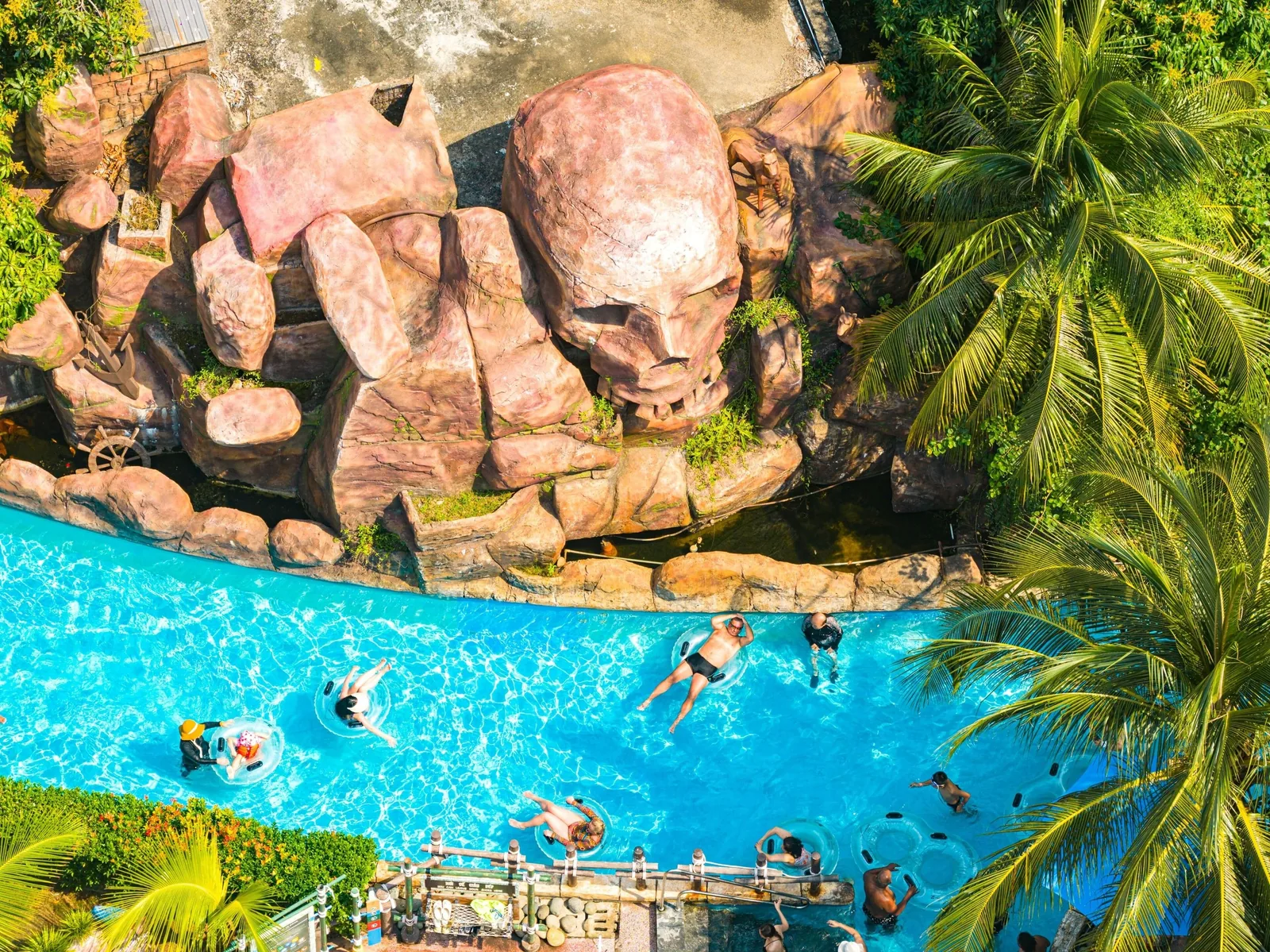 Aerial view of visitors floating in a lazy river beside rocky formations at Aquatopia water park on Hon Thom, Phu Quoc.
