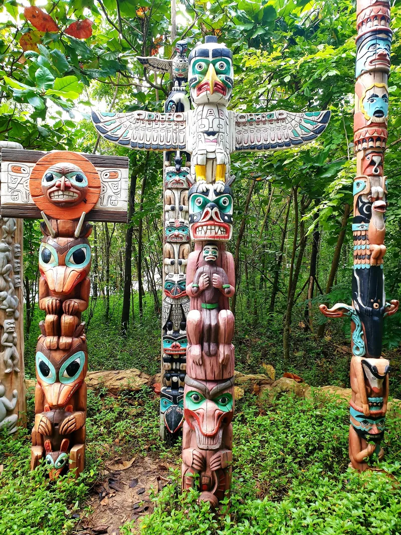 Colorfully carved totem poles with animal and human figures stand among greenery in a Phu Quoc park.