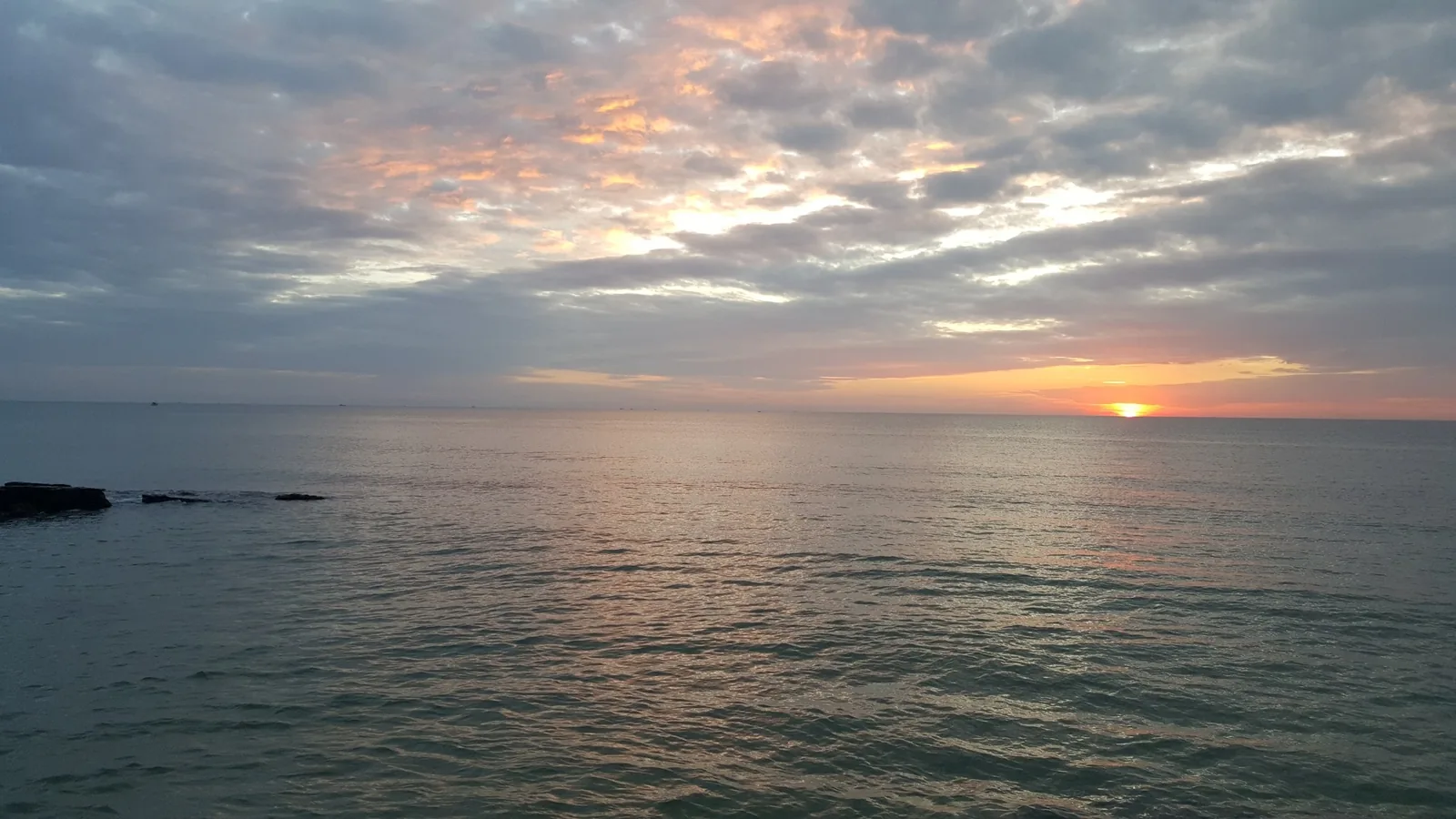 Sun setting over the calm sea at Phu Quoc, with orange light spreading across a cloudy sky.