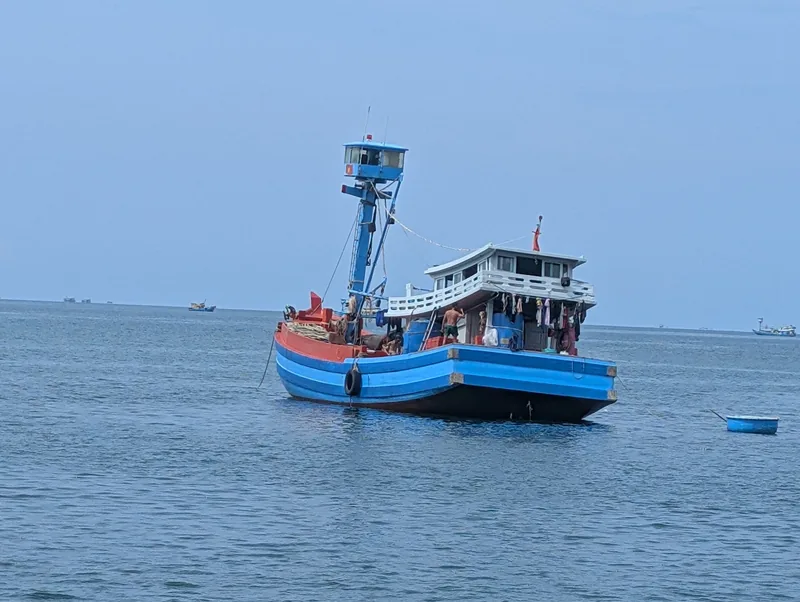 A blue wooden fishing boat with laundry hanging from its rails floats calmly on the sea off Phu Quoc.