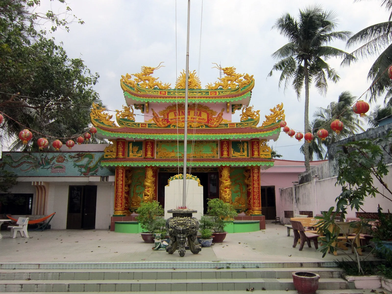 Colorful dragon-adorned roof and ornate facade of Dinh Cau shrine on Phu Quoc, with red lanterns and palm trees.
